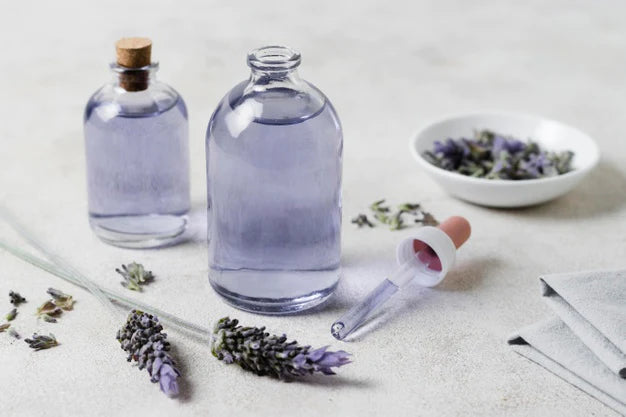 Two Bottles of lavender oil, lavender leaves, lavender leaves in bowl and dropper kept with two piece of cloth | levender oil for hair
