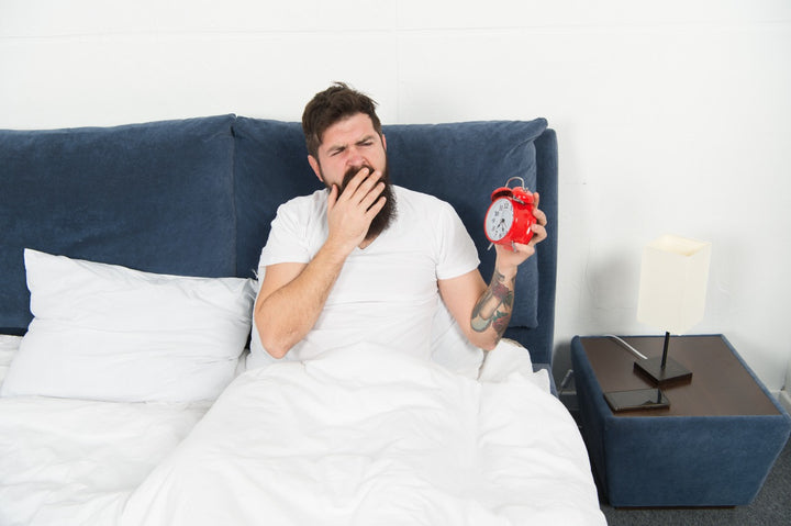 Man yawning on bed and holding clock | benefits of nightfall