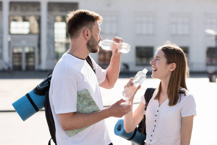 a man and a woman drinking water while they are holding bags